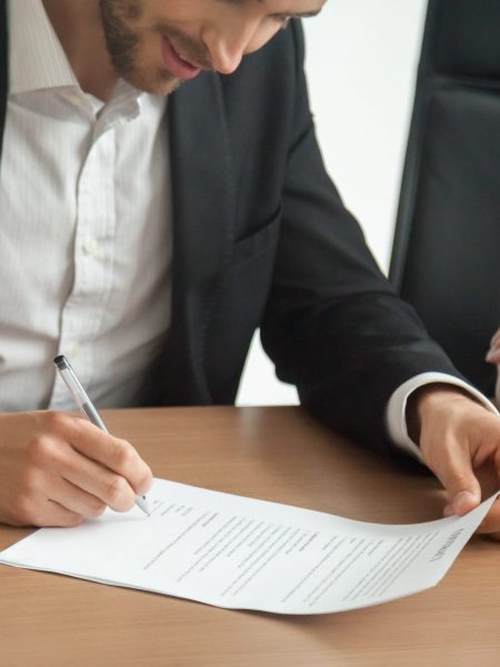 Satisfied smiling businessman in suit signing contract at meeting concept, investor or entrepreneur putting written signature on business document making good partnership deal, taking loan insurance